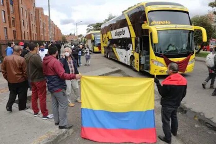 Transportadores permanecen junto a sus buses con la bandera de Colombia durante una movilización realizada este miércoles por las calles de Bogotá. EFE / Carlos Ortega